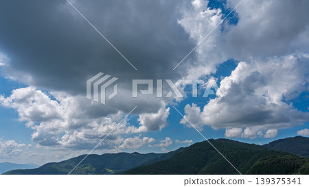 Many white clouds drift across the bright blue summer sky, and the mountains are covered in green. Many white clouds drift across the bright blue summer sky, and the mountains are covered in green. 139375341