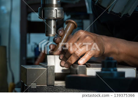 Professional machine operator setting up metal workpieces on an NC milling machine using a copper hammer for precision adjustment. 139375366