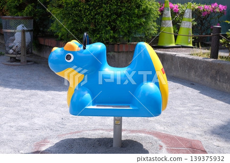 公園裡有一個藍色的翼龍形狀的彈簧遊樂設施;一個戶外兒童搖晃恐龍遊樂場。 公園裡有一個藍色的翼龍形狀的彈簧遊樂設施;一個戶外兒童搖晃恐龍遊樂場。 139375932