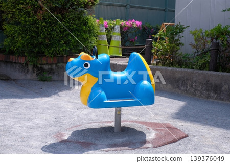 公園裡有一個藍色的翼龍形狀的彈簧遊樂設施;一個戶外兒童搖晃恐龍遊樂場。 公園裡有一個藍色的翼龍形狀的彈簧遊樂設施;一個戶外兒童搖晃恐龍遊樂場。 139376049
