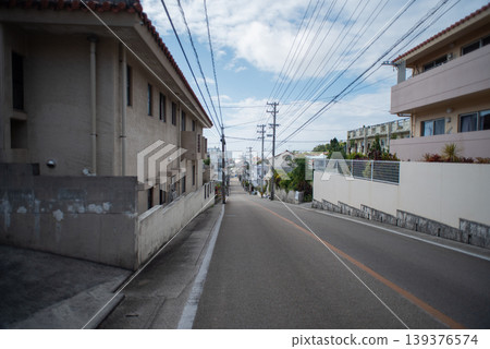 A straight, gently sloping road in a residential area with a view of the town in the distance. 139376574