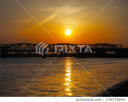 The silhouette of the Arakawa Railway Bridge against an orange sunset. The silhouette of the Arakawa Railway Bridge against an orange sunset. 139376844