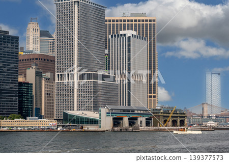 New york, usa august 16,2024. New york city skyline with financial district skyscrapers and staten island ferry terminal building, a boat traveling on the water New york, usa august 16,2024. New york city skyline with financial district skyscrapers and staten island ferry terminal building, a boat traveling on the water 139377573