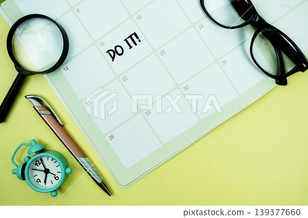 Do it! message written on calendar date with alarm clock, glasses and magnifying glass on yellow background 139377660