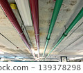 pipes mounted along a concrete ceiling in an industrial facility, perspective lines leading through underground space, infrastructure system details with lighting, modern engineering concept, utility 139378298
