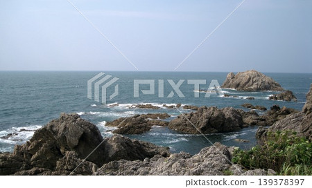 Blue sky, blue sea, white waves crashing against strangely shaped rocks, and green plants growing on the rocks. Blue sky, blue sea, white waves crashing against strangely shaped rocks, and green plants growing on the rocks. 139378397