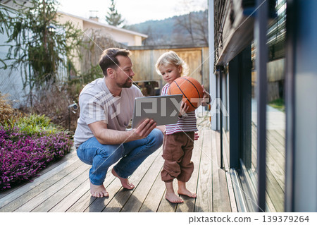 Father controlling smart home exterior blinds using tablet while standing with toddler son. 139379264