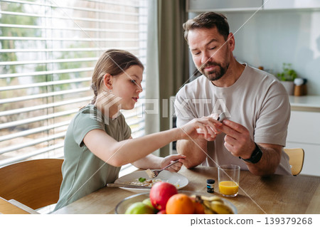 Father checking blood sugar level of diabetic teenage daughter using glucose meter. Father checking blood sugar level of diabetic teenage daughter using glucose meter. 139379268