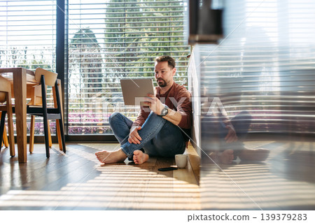 Man using smart home app working on tablet and sitting on floor. Man using smart home app working on tablet and sitting on floor. 139379283