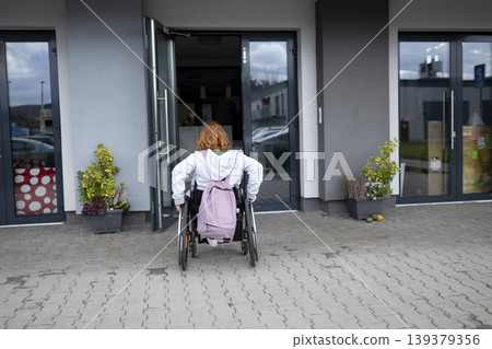 Woman in wheelchair entering modern building with accessible entrance. 139379356