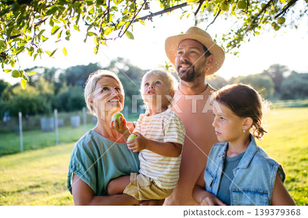 Family on walk in summer nature, standing under apple tree. 139379368