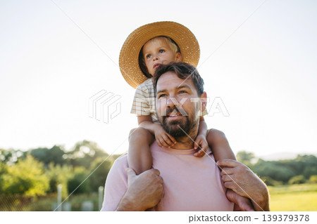 Dad carrying little boy on shoulders during warm summer day. Dad carrying little boy on shoulders during warm summer day. 139379378