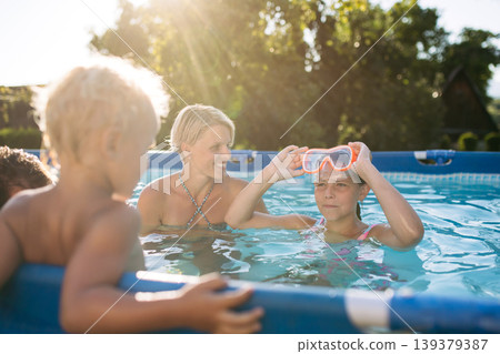 Young family with two children in swimming pool outdoors in backyard garden. Young family with two children in swimming pool outdoors in backyard garden. 139379387