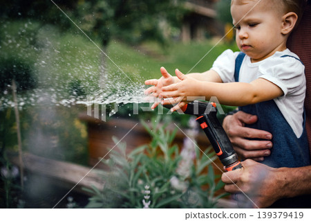 Close up of kid playing and watering plants with hose. Close up of kid playing and watering plants with hose. 139379419