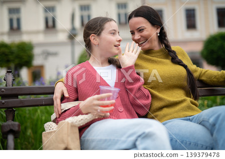 Mother and daughter sitting on park bench, talking. Mother and daughter sitting on park bench, talking. 139379478