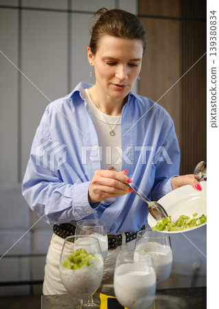 Woman prepares dessert using yogurt and fruits in modern kitchen during afternoon time Woman prepares dessert using yogurt and fruits in modern kitchen during afternoon time 139380834