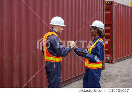 Caucasian male and Black female logistics workers in solidarity handshake at Asian shipping port. Caucasian male and Black female logistics workers in solidarity handshake at Asian shipping port. 139381037