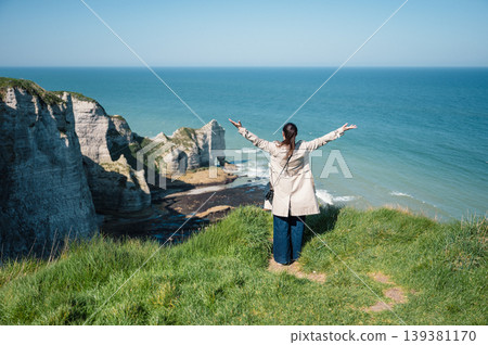 Woman stands and look at cliffs and Waters of Etretat 139381170