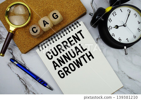 CAG Current Annual Growth text written on notepad with magnifying glass and alarm clock on marble background CAG Current Annual Growth text written on notepad with magnifying glass and alarm clock on marble background 139381210