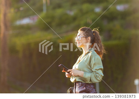 Modern Woman Holding Smartphone During Sunset Relaxation Modern Woman Holding Smartphone During Sunset Relaxation 139381973