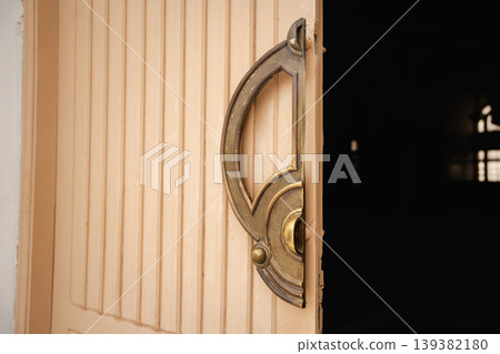 Wooden mosque entrance door with ornate brass door handle partially open showing dark interior space. Islamic architecture entrance detail 139382180