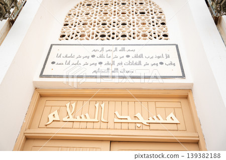 Mosque entrance with arabic calligraphy inscription panel above door and geometric mashrabiya ventilation screen. Islamic architecture and religious text Mosque entrance with arabic calligraphy inscription panel above door and geometric mashrabiya ventilation screen. Islamic architecture and religious text 139382188