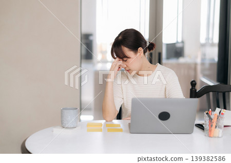 Stressed tired asian woman suffering headache working on laptop at desk with problem in home office feeling exhausted looking overworked and drained rubbing face 139382586