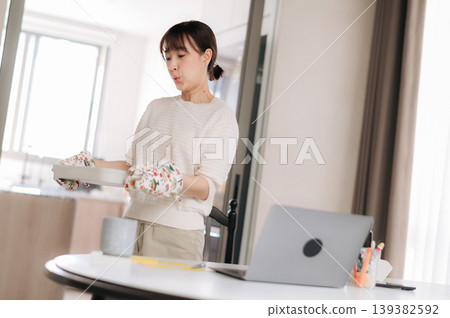 Young asian woman stands near table holding floral arrangement looking focused towards laptop computer screen in bright contemporary apartment living room space Young asian woman stands near table holding floral arrangement looking focused towards laptop computer screen in bright contemporary apartment living room space 139382592