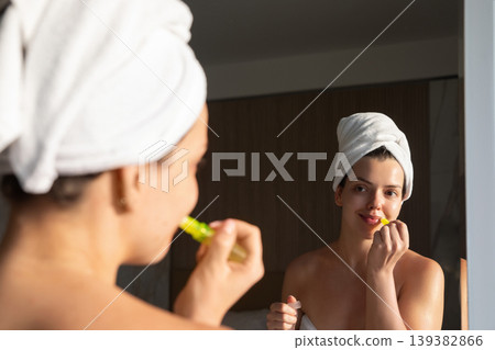 Beautiful woman applying lip balm in mirror after shower, beauty skincare routine with natural glow and smooth skin, female model enjoying wellness selfcare lifestyle in warm sunlight indoor setting Beautiful woman applying lip balm in mirror after shower, beauty skincare routine with natural glow and smooth skin, female model enjoying wellness selfcare lifestyle in warm sunlight indoor setting 139382866