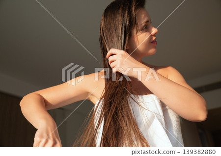 Pretty woman brushing long wet hair after drying, beauty haircare routine indoors, female model with natural skin and relaxed pose, wellness and healthy lifestyle concept 139382880