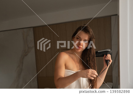 Attractive woman drying long wet hair with hair dryer in front of mirror healthy shiny hair beauty routine indoor portrait Attractive woman drying long wet hair with hair dryer in front of mirror healthy shiny hair beauty routine indoor portrait 139382898