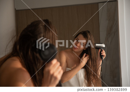Young woman drying long wet hair with hair dryer and looking in mirror reflection healthy smooth hair beauty routine portrait 139382899