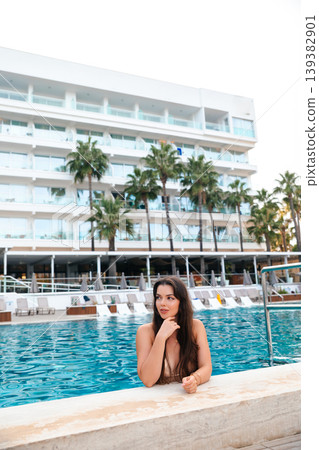 Beauty woman resting chin on hand by poolside at modern resort with palm trees enjoying summer vacation lifestyle and calm beauty relaxation in warm sunlight Beauty woman resting chin on hand by poolside at modern resort with palm trees enjoying summer vacation lifestyle and calm beauty relaxation in warm sunlight 139382901