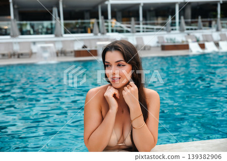 Beauty portrait of woman near pool touching chin and smiling enjoying summer vacation luxury resort lifestyle with blue water and beauty skincare sun protection Beauty portrait of woman near pool touching chin and smiling enjoying summer vacation luxury resort lifestyle with blue water and beauty skincare sun protection 139382906
