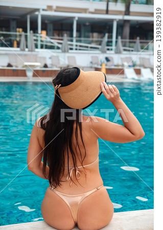Female model seen from back in bikini and straw hat entering pool enjoying summer vacation resort lifestyle beauty scene with blue water and relaxed mood 139382919