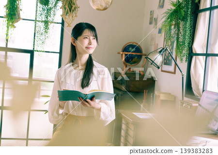 一位年輕的日本女子在家裡的房間裡微笑著,手裡拿著筆記本。 一位年輕的日本女子在家裡的房間裡微笑著,手裡拿著筆記本。 139383283