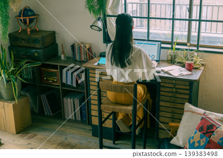 The back view of a young Japanese woman sitting at her desk at home. The back view of a young Japanese woman sitting at her desk at home. 139383498