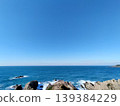 A view of the sea crashing against the rocks under a blue sky. 139384229