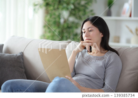 Thoughtful asian woman reading carefully a document at home 139385734