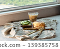 Bathed in the glow of a sun-drenched window, this artisanal breakfast is a study in texture and light. At its heart lies a golden-brown pastry, its cheese-dusted crust blistered to a perfect, savory 139385758