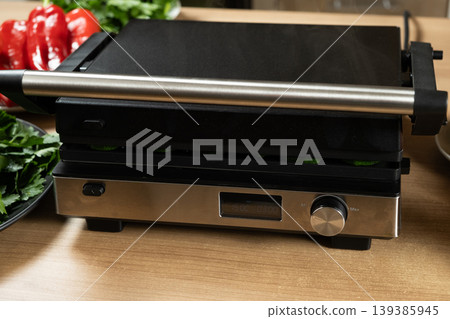 Modern Electric Contact Grill on Kitchen Wooden Table Background Modern Electric Contact Grill on Kitchen Wooden Table Background 139385945