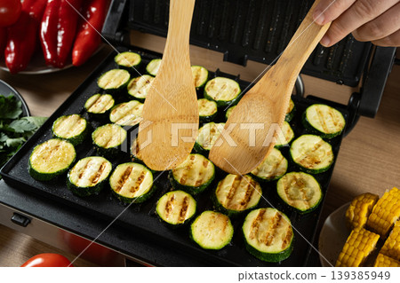 Flipping Grilled Zucchini Slices with Wooden Spatulas on Electric Grill Flipping Grilled Zucchini Slices with Wooden Spatulas on Electric Grill 139385949