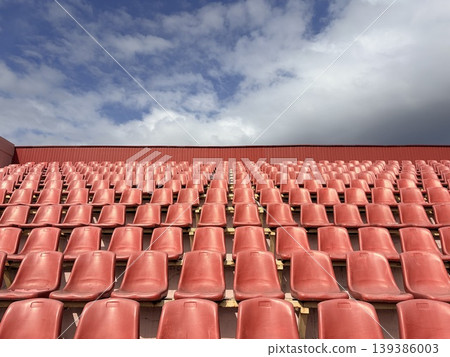 rows of red plastic seats at an open-air sports stadium. Sports arena sporting competition 139386003