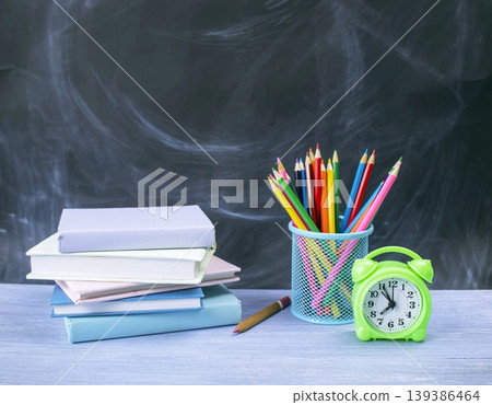 School supplies with books, pencils and alarm clock on the table against a blackboard background, back to school concept. 139386464