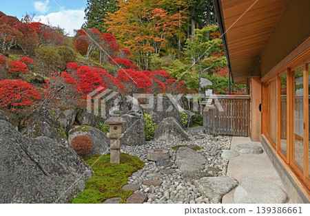 A stone garden bathed in crimson light; a charming stone lantern and enkianthus shrubs create a beautiful Japanese autumn scene. 139386661