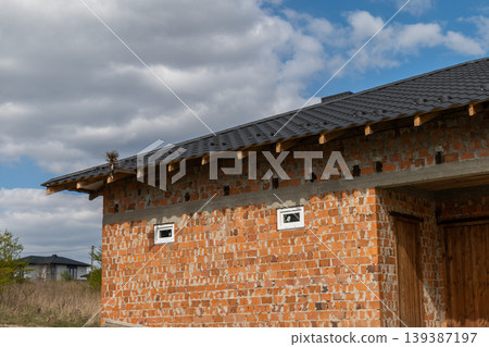 House features black metal tiles on the roof and brick walls in a grassy area with trees under a partly cloudy sky 139387197