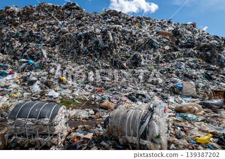 Workers and machines gather waste at a municipal trash site filled with heaps of garbage under a blue sky 139387202