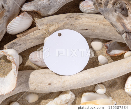 Blank round gift tag mockup on sand near seashells and driftwood with hard shadows, label design Blank round gift tag mockup on sand near seashells and driftwood with hard shadows, label design 139387284