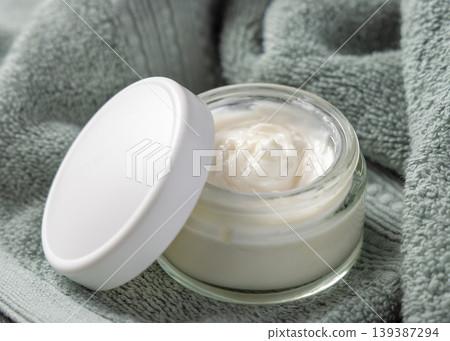 Opened cream glass jar mockup with a blank lid on sage green bath towel closeup. Cosmetic packaging 139387294