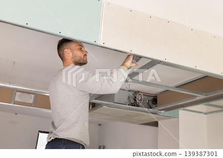 Construction worker installs metal profile frame for drywall suspended ceiling system in apartment Construction worker installs metal profile frame for drywall suspended ceiling system in apartment 139387301